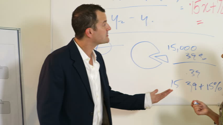 Camera pans down from an instructor and pretty female student standing at whiteboard to male student writing in notebook. 
