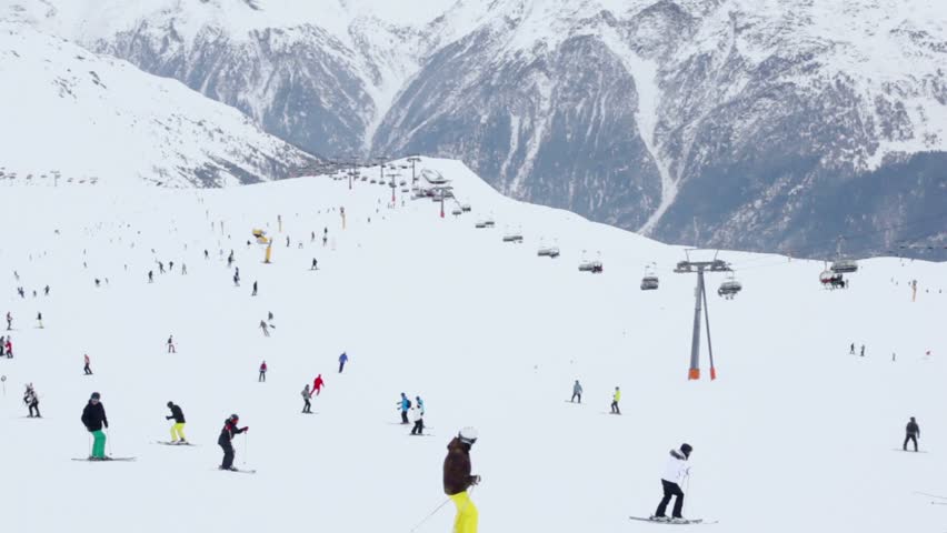 Lot of skiers ride in Alps near ropeway at sunny winter day