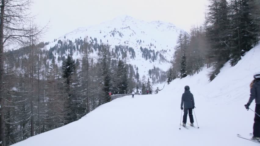 Several people ride ski by snow slope among forest at mountains, riders view in motion