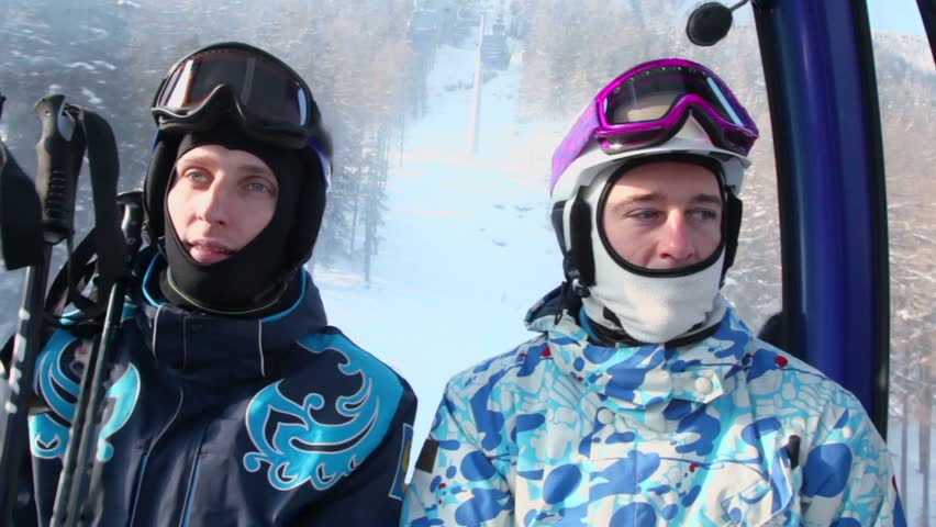 Two skiers in helmets ride on funicular at mountains