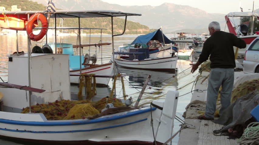 LITTLE PORT VATHI, MEGANISI/GREECE - OCTOBER 1:  Unidentified fisherman stands next to his fishing boat and mends his nets in the early morning on October 1, 2012 in Little Vathi.