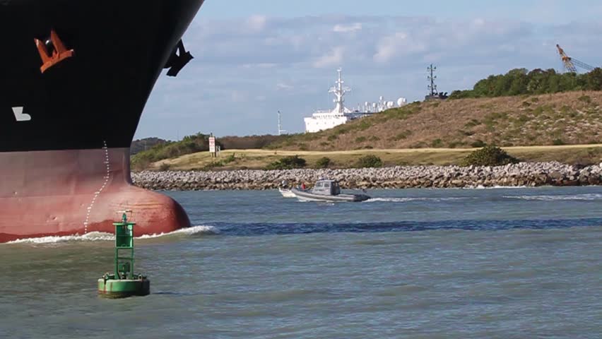 Cargo ship passing a buoy as the ship exits Port Canaveral, Florida. Clip starts with  close-up of ship's bow passing a harbor marker buoy, then pans the length of the ship, ending at the bridge.