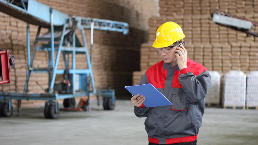 Man working in Warehouse, controlling and writing the results of the quality and number of bags in a sugar refinery, He's talking on cellphone