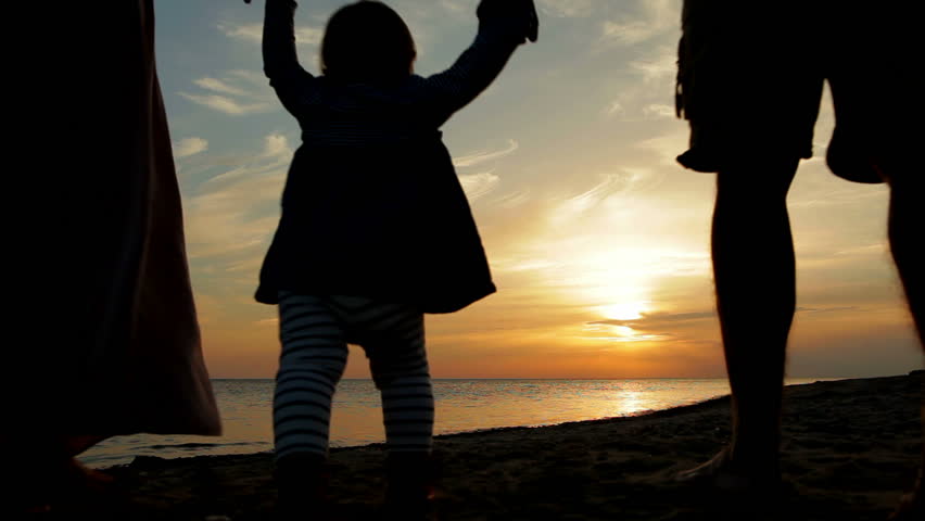 Happy family walking on sea coast. Silhouettes sunset.