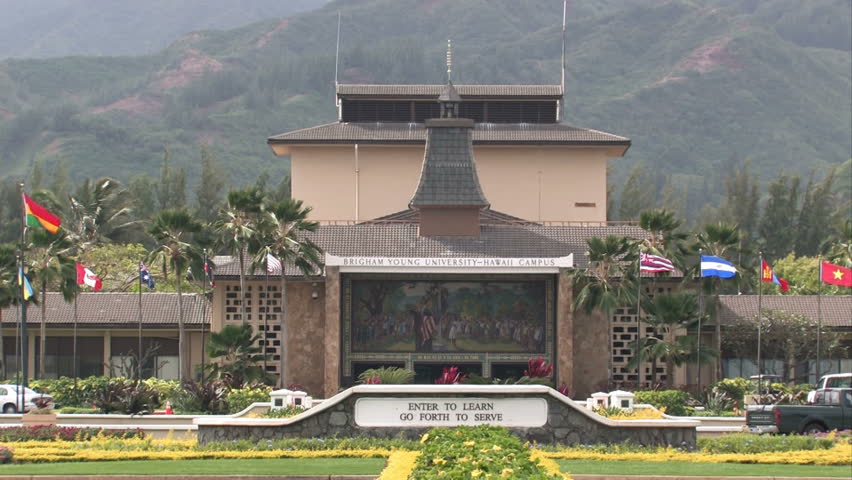 Campus of Brigham Young University, BYU, in Oahu Hawaii. Front entrance road with flowers and tropical palm trees. Flags of various nations flying.Zoom out to flowers.