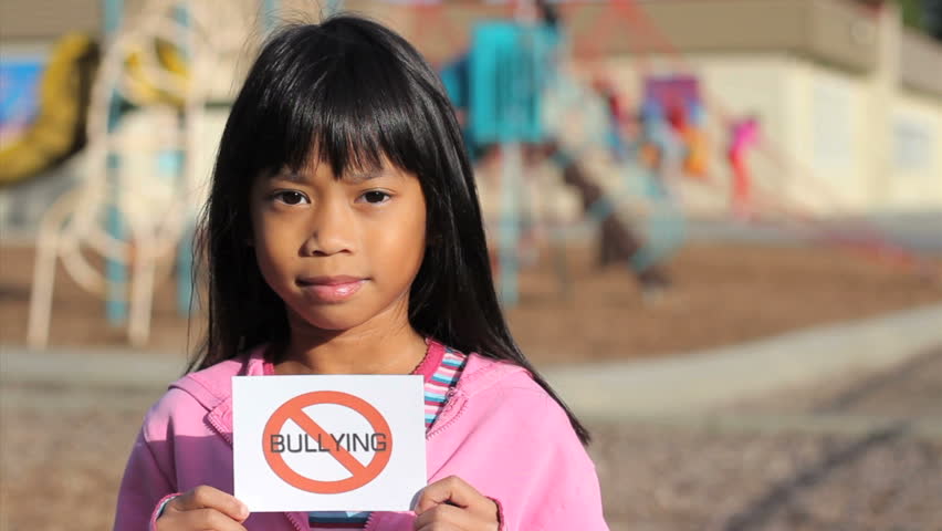 A cute Asian girl holds up a "NO BULLYING" sign on the school playground.