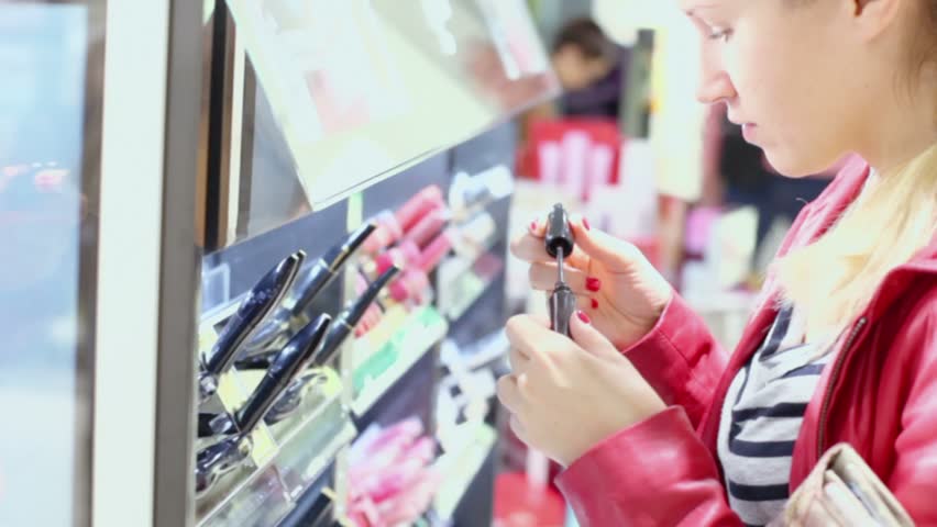 Young woman with braid smells mascara in small shop
