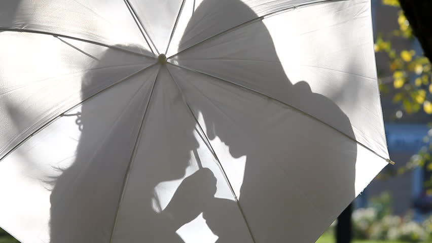 Young lovers couple shadows hugging and kissing behind an white umbrella against the light