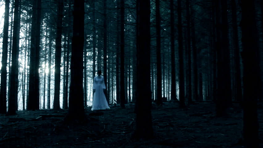 Mysterious woman in white dress in dark spooky forest