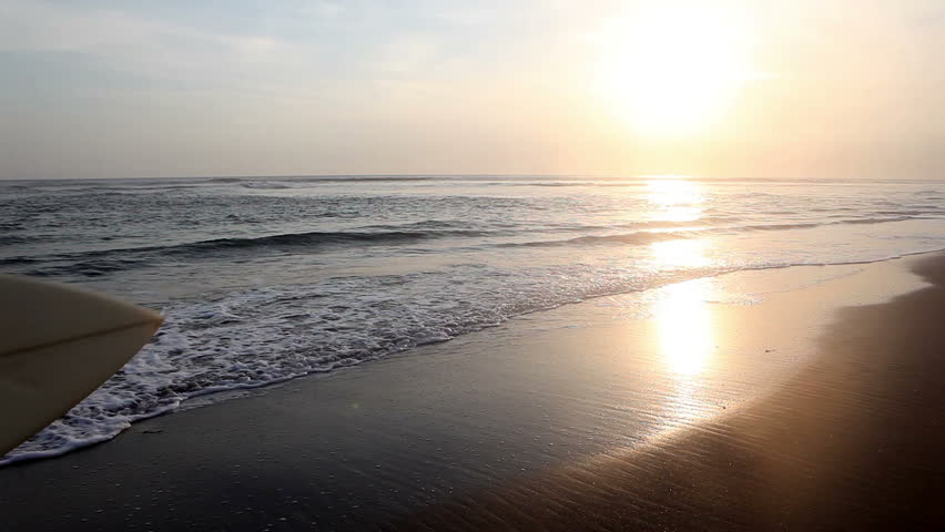 Surfer holding surf board and on coast Bali during sunset