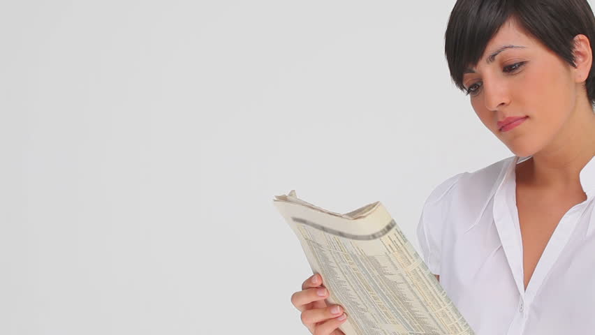 Businesswoman nods as she reads a newspaper against a grey background