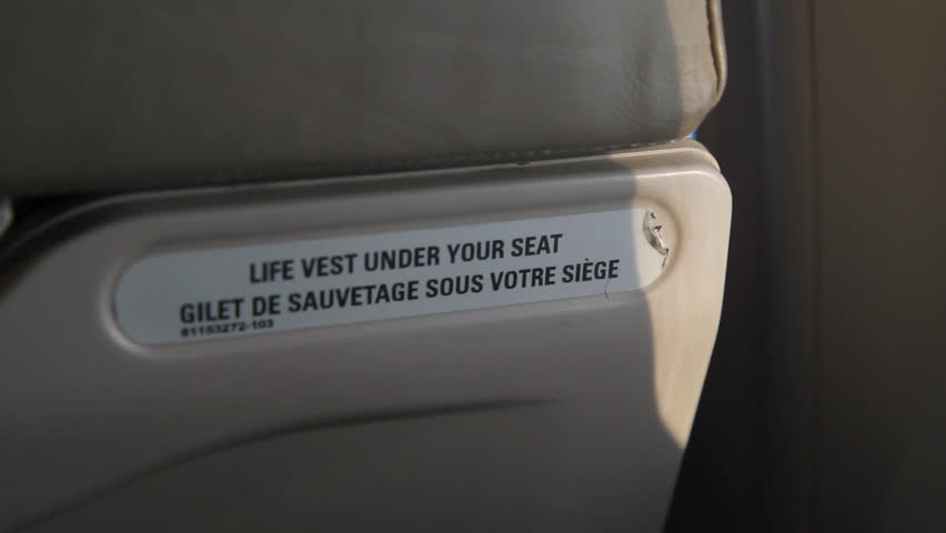 Detail of plane seat with âLife vest under your seatâ notice. Rack focus at end of shot. Inflight on a commercial turboprop plane.