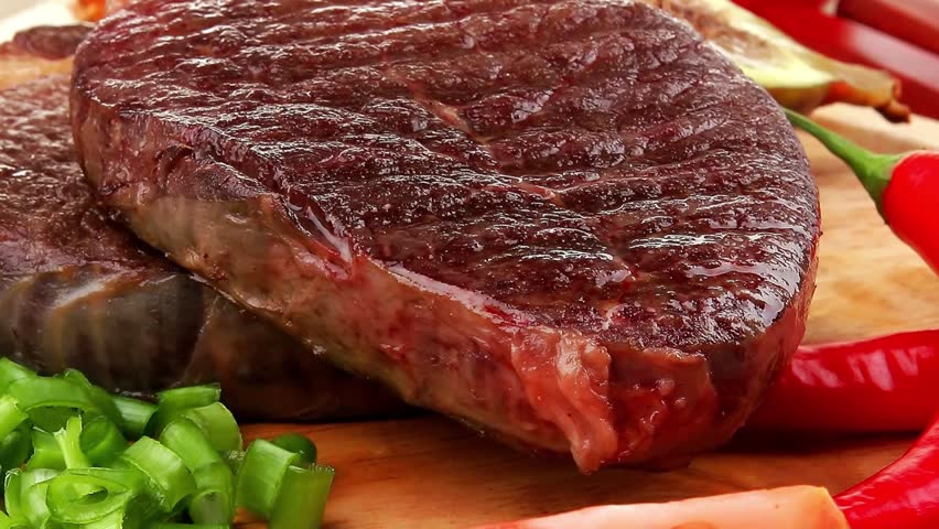 meat entree : grilled beef steak served with red hot cayenne peppers green stuff sweet figs and cutlery on wood plate over wooden table