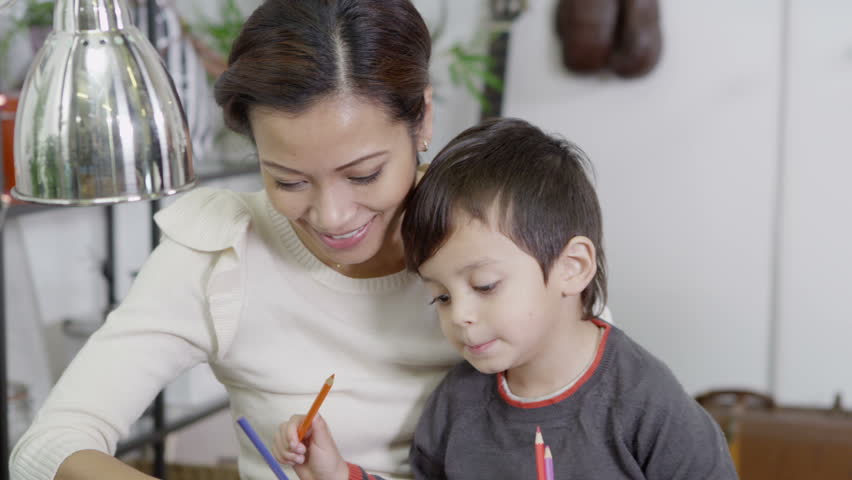 A mother and her cute young son spend time together at home, drawing and writing with colored pencils. In slow motion.