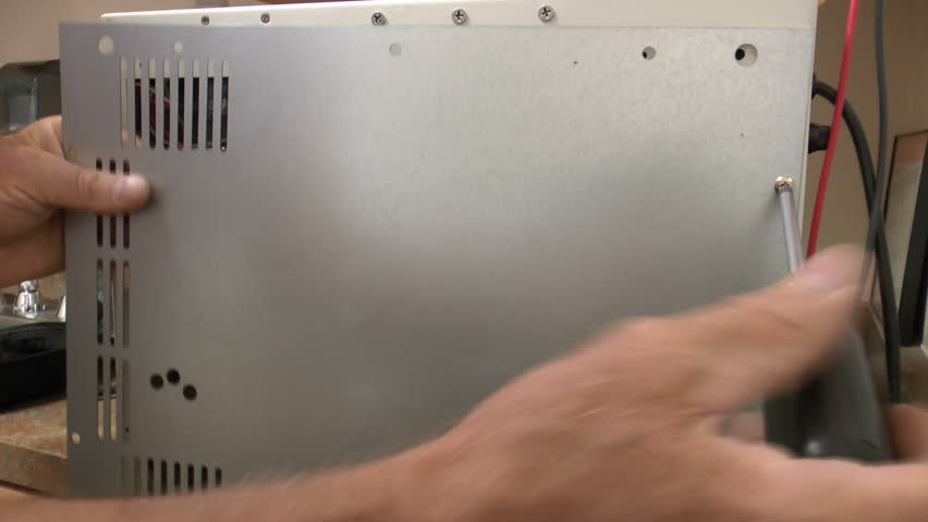 Biomedical equipment technician unscrews back plate off medical equipment centrifuge unit, troubleshoots printed circuit board with voltmeter. 1080p
