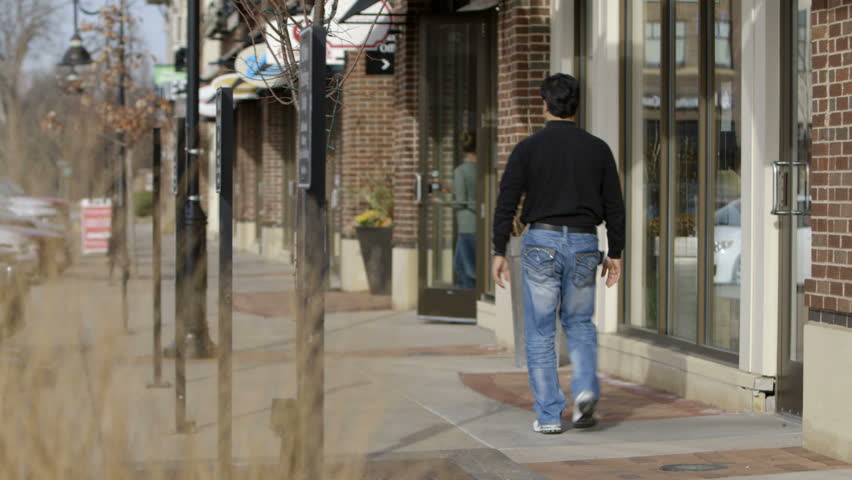 Shopping scene, with pedestrians walking past and exiting from a row of stores.