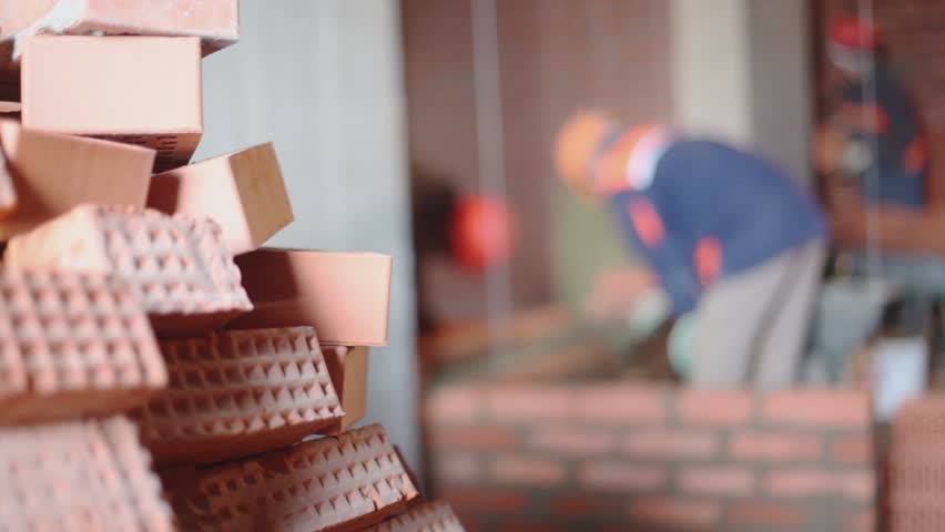 Stack of bricks at background of few workers build wall unfocused