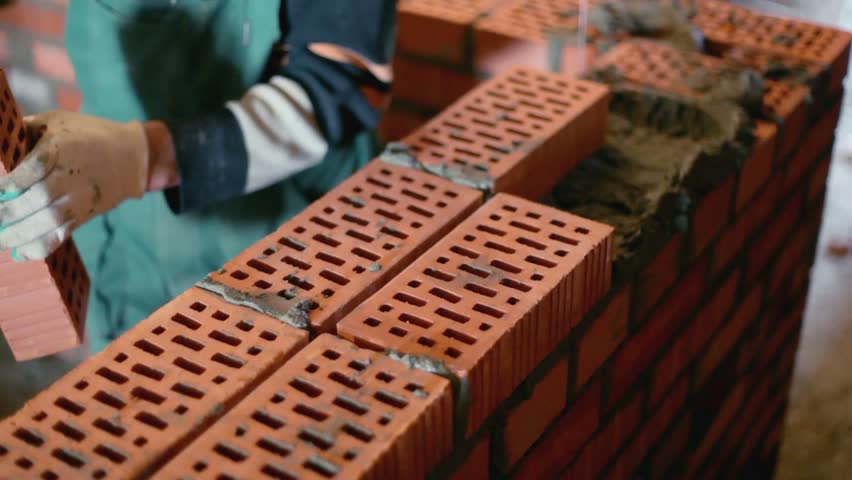 Labourer lays bricks during brickwork with trowel, closeup view at construction site