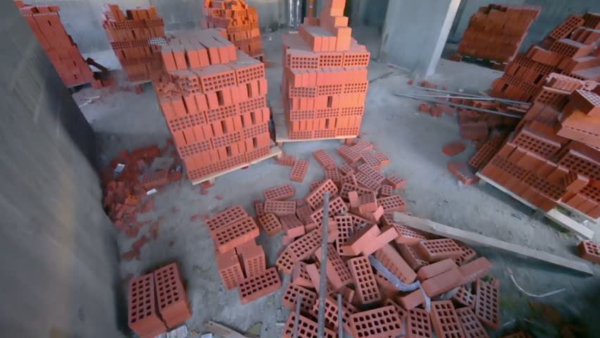 Stacks of red bricks inside unfinished room, shown in motion