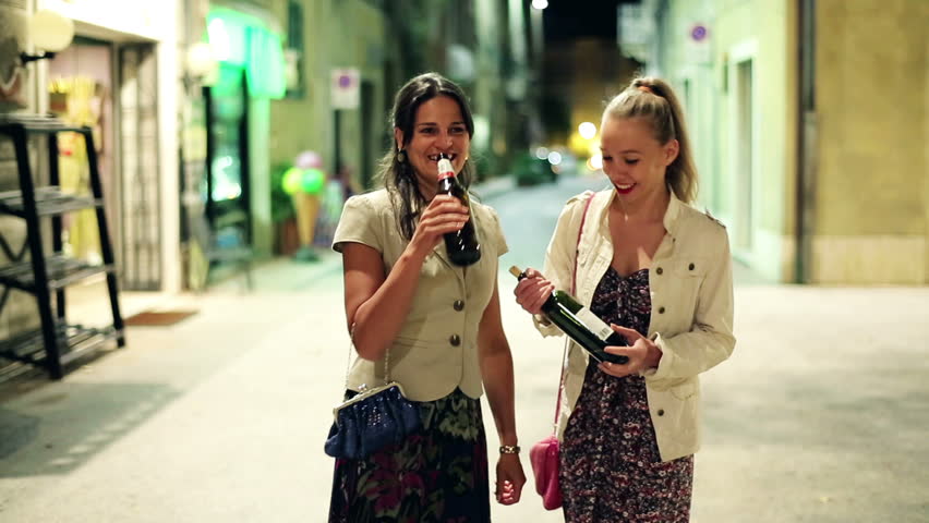 Drunk women with bottle of vine standing on the street in the evening, stabilized shot