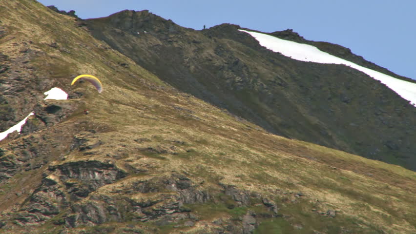 Reverse zoom pullback from tight tele shot of a paraglider soaring at Hatcher Pass in Alaska, revealing another paraglider high above.