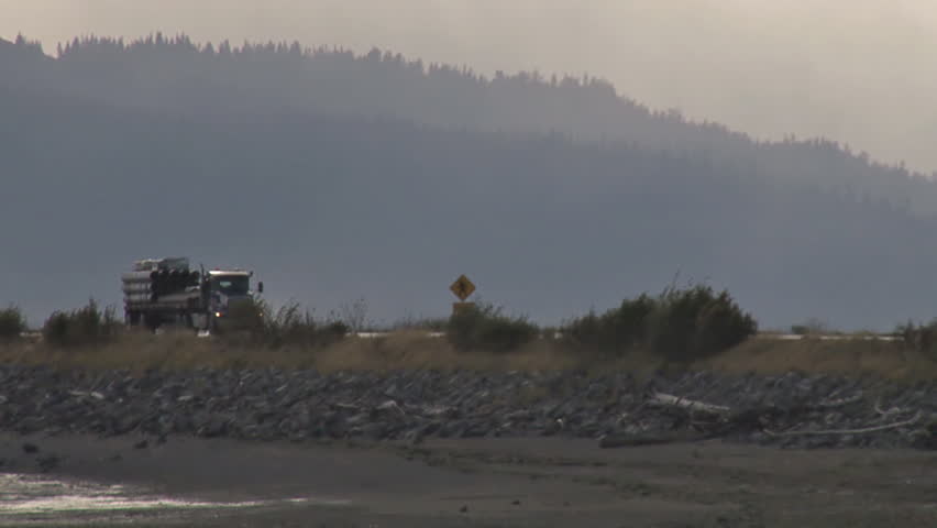 Long shot of a tractor trailer moving along a levy on a cloudy day.