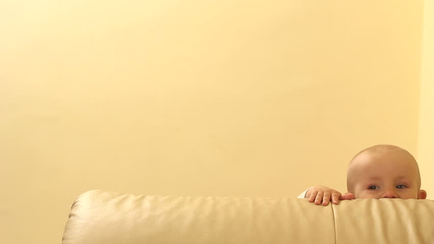 Baby rising up alone on the edge of the couch