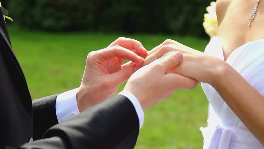 closeup of bride and groom exchainging wedding rings over green nature background
