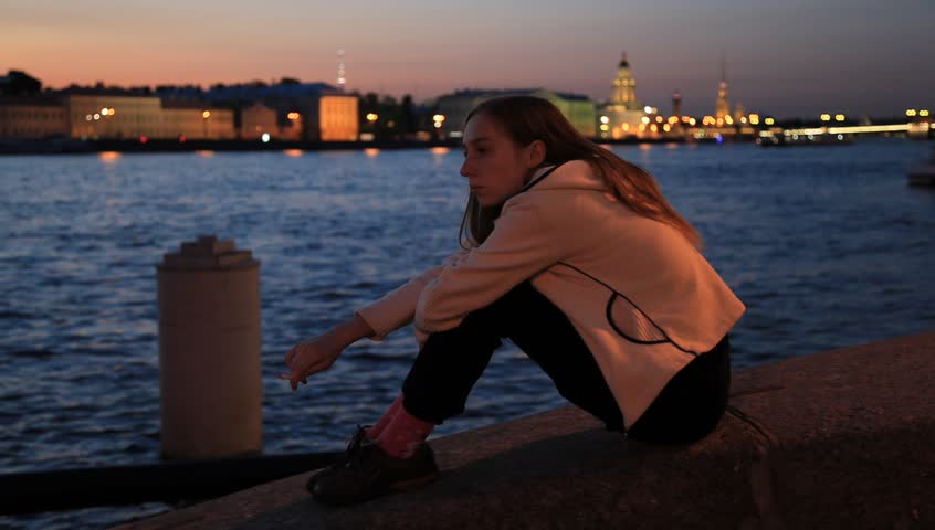Tired girl sits and smokes on the waterfront at white night in St. Petersburg, Russia. The focus changing to architectural background at the end. 1080p
