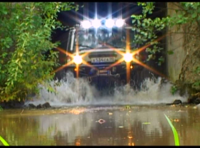 Off - road vehicle crossing the river in East Europe. Splashes of water from under weels. Slow motion