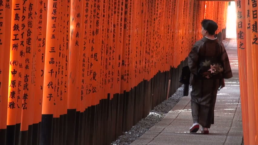 KYOTO, JAPAN - 22 OCTOBER 2012: A woman in Japanese geisha clothing walks through torii gates at Fushimi Inari in Kyoto, Japan