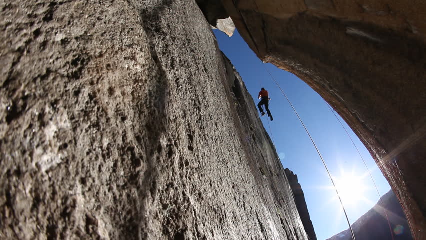 A silhouette of a female rock climber with safety harness and rope attempts to climb a boulder during the day in a national park