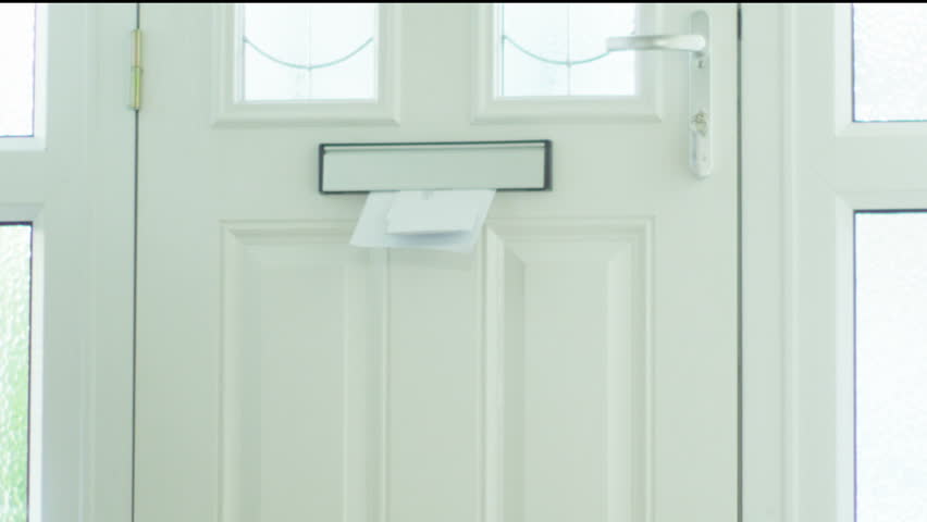 Letters and bills dropping through the letter box of a house and landing on the mat