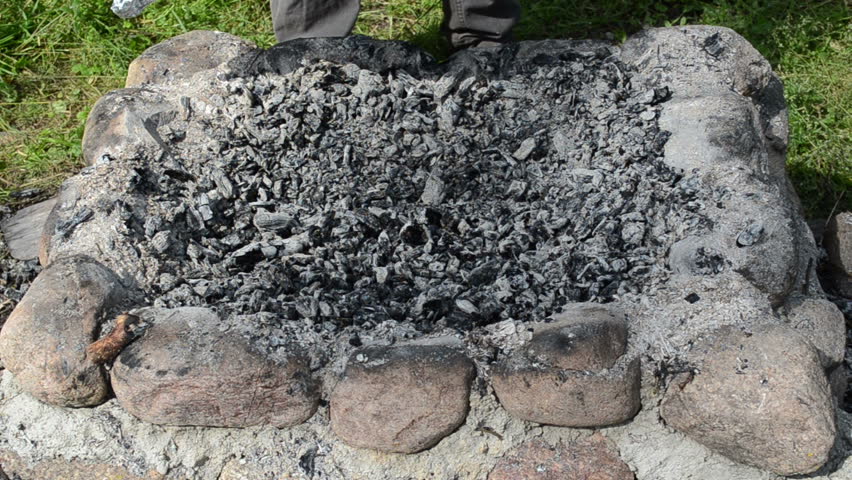 man hand put huge fish wrapped foil put into fire bonfire and bury with ember cinder.