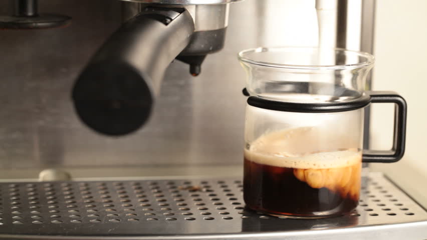 Coffee maker pouring hot milk foam in espresso to prepare coffee with milk