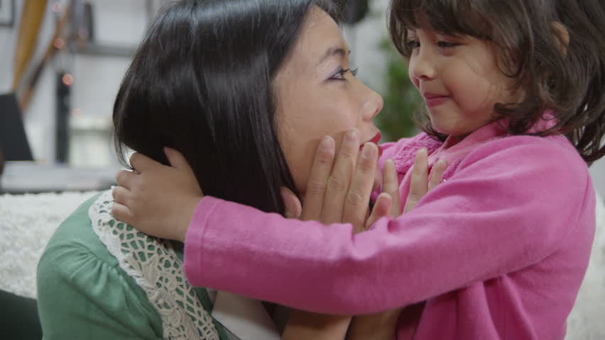A woman is upset and worrying about events in her life which are beyond her control. Her small daughter comes to her to give her a hug and to smile at her to cheer her up. In slow motion.