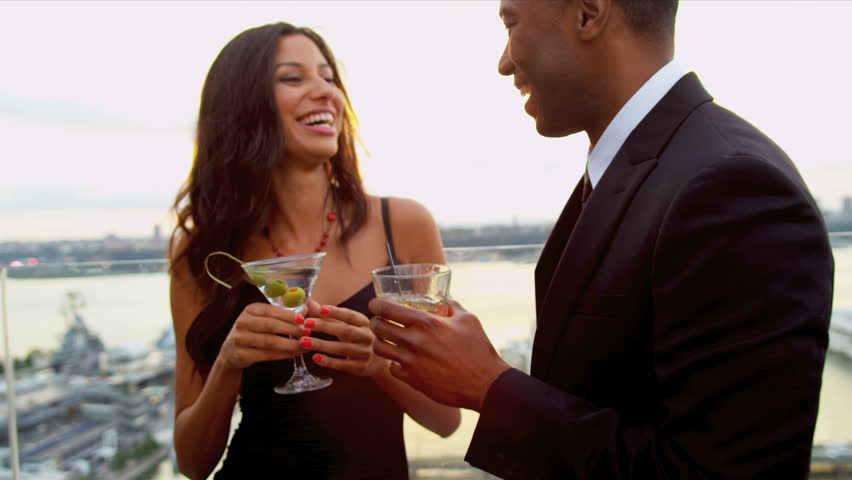 Happy multi ethnic couple taking and drinking at city roof cocktail party dressed in black