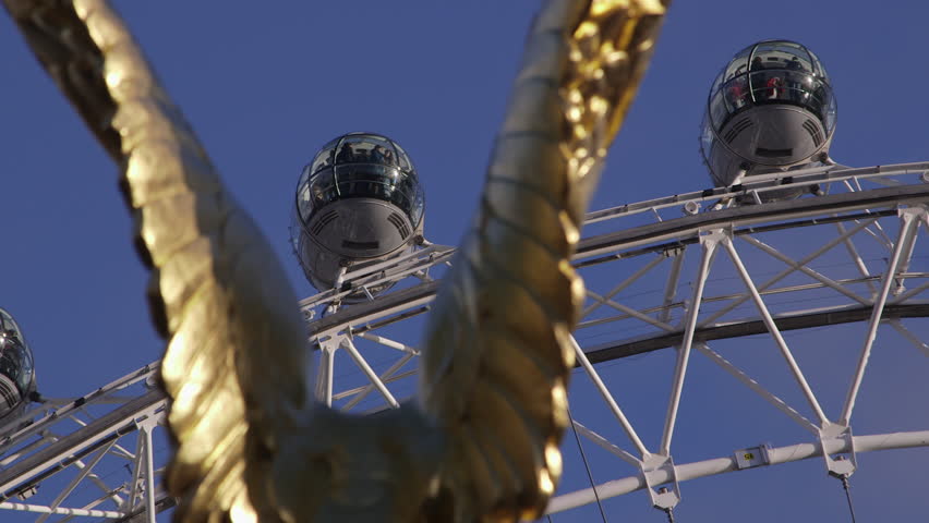 LONDON - CIRCA 2013: Closeup shot of the top of The London Eye pods seen through the wings of gold covered eagle of The RAF Memorial on The Embankment. Each pod is moving across the wing to the right