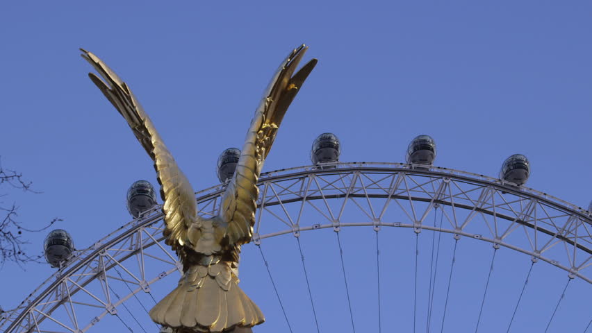 LONDON - CIRCA 2013: Mid shot of the top of The London Eye pods seen through the wings of the gold covered eagle perching on the summit of The RAF Memorial on The Embankment