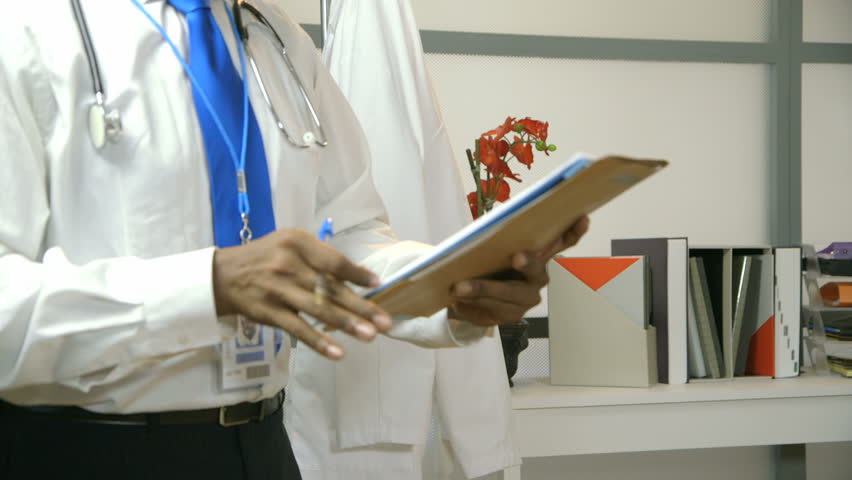 A doctor or surgeon sitting in front of a laptop shows fatigue as he removes his stethoscope and cap as if calling it a day. 