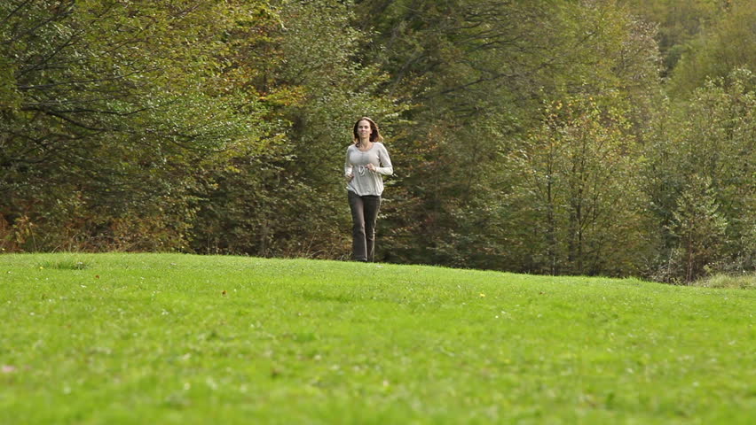 Girl running from the woods across the green grassy field toward camera