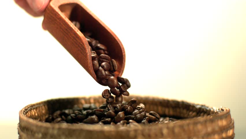 Coffee beans pouring from wooden scooper held by hand in slow motion