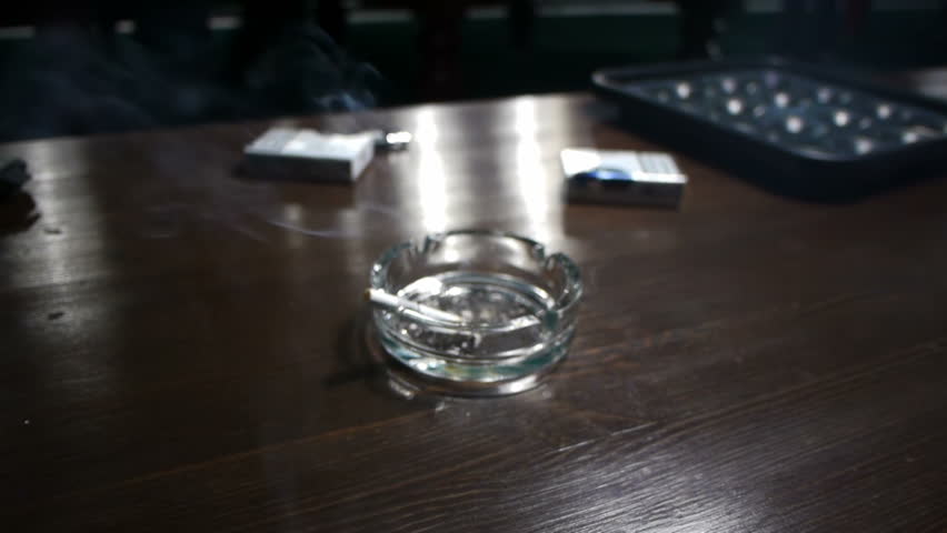 Ashtray with smoking cigarette in a pool room (shallow DOF)