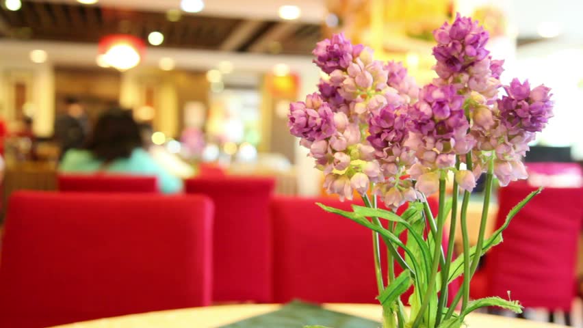 Artificial purple lilies in a square glass vase on the table in the hotel restaurant