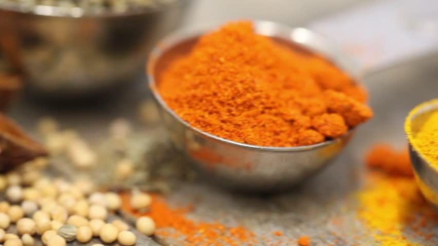 Various mixed spices (oregano, curcuma, paprika, anise) in metal scoops on wooden table