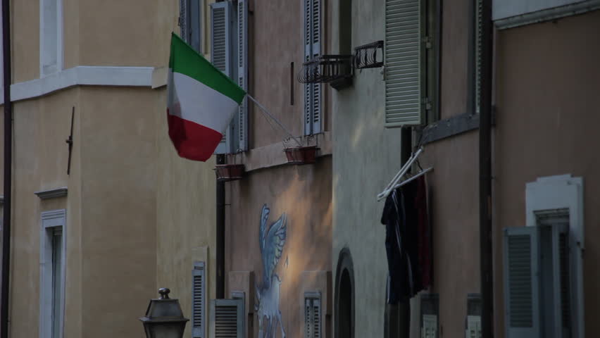 Walls and windows of a quiet Italian street. An Italian flag is prominently displayed from a windowsill.
