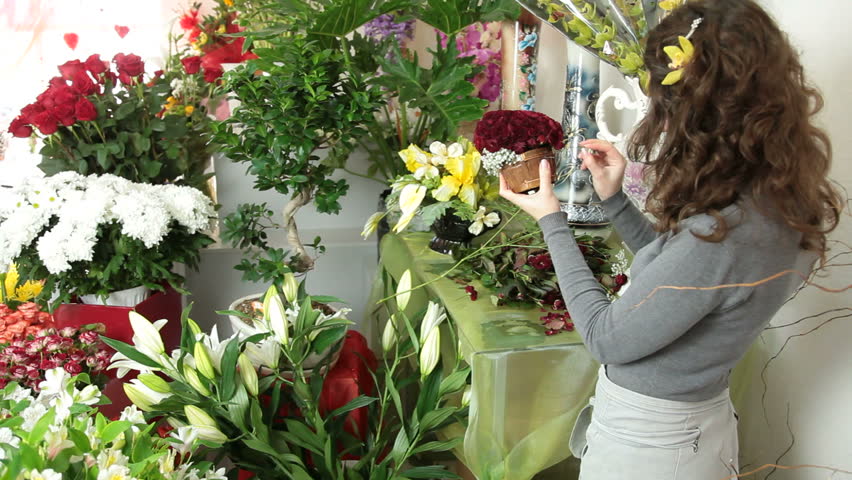 Florist arranging rose heart-shaped bouquet is surrounded by gypsophila in flower shop. Medium shot