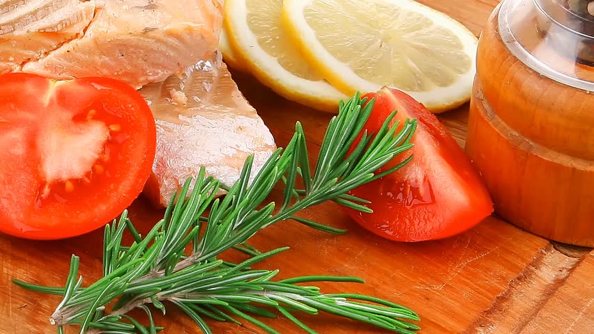 sea food : roasted pink salmon fillet with chinese onion cherry tomatoes pieces pepper grinder rosemary twigs and lemon on wooden board hidef slow motion intro