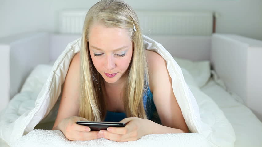 A young woman lying on the bed and using smart phone.