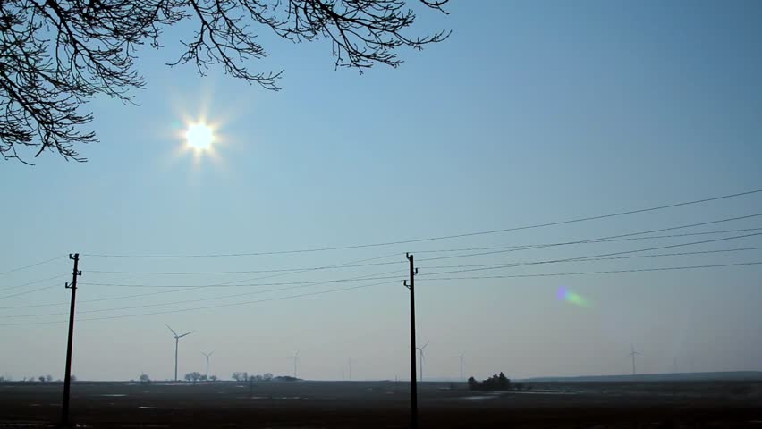 Electricity network in a bright sunny day. Wind turbines producing green energy in the background. Northeast Bulgaria.